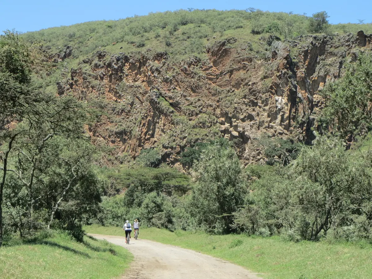 Grindpad met twee fietsers onder groene hellingen en een rotswand in Hell's Gate