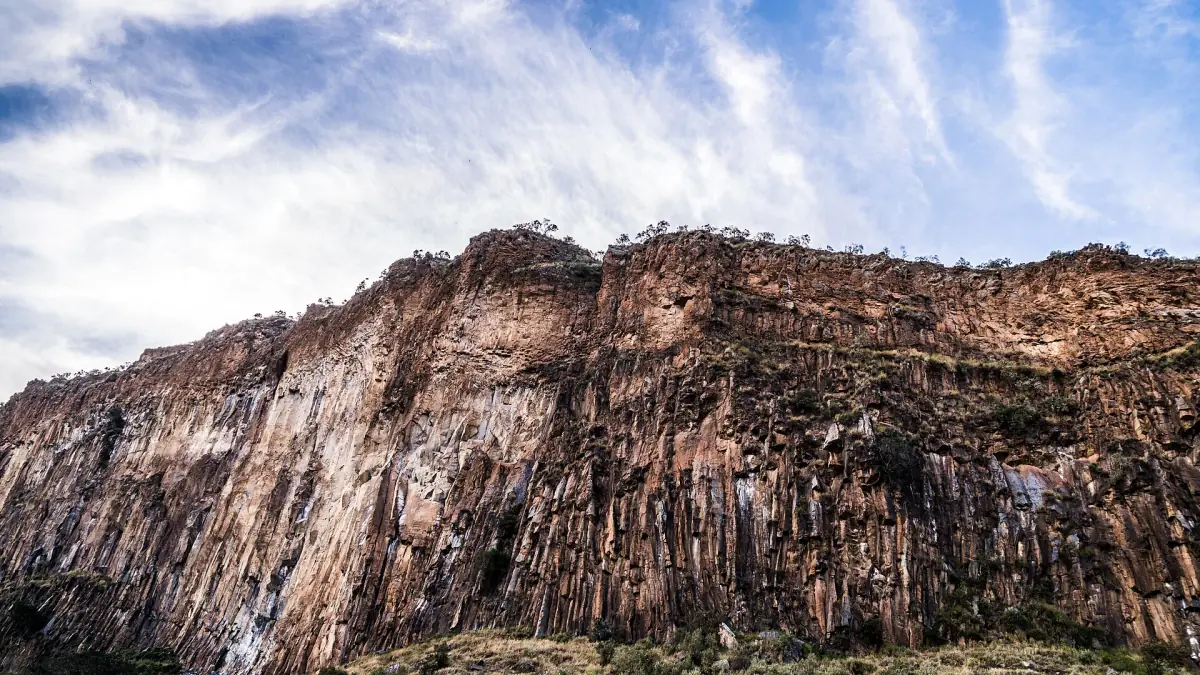 Layered volcanic cliff wall under wispy clouds in Hell's Gate National Park