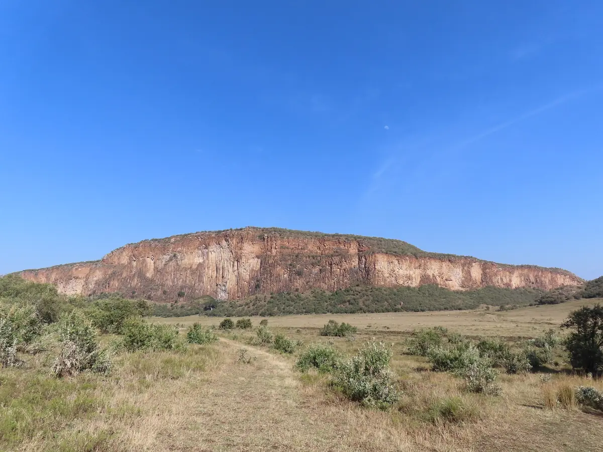 Long reddish cliff above dry grassland under a deep blue sky
